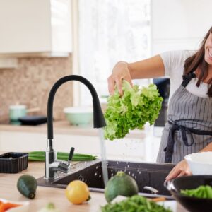 Cheerful attractive Caucasian woman in apron washing salad in ki